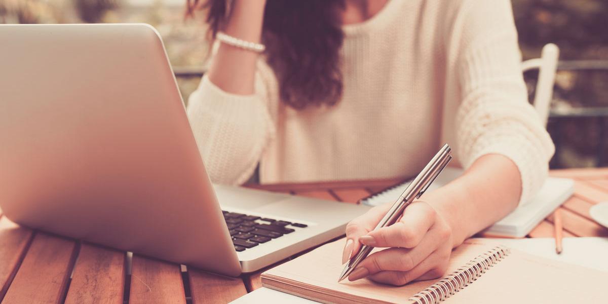 Female student looking at laptop and taking notes on paper.